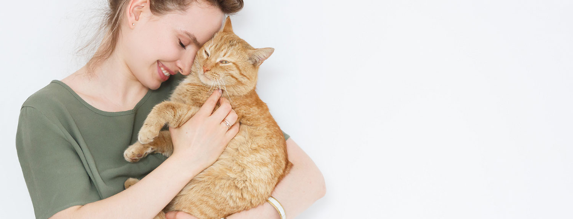 woman holding an orange cat lovingly in her arms on a white background